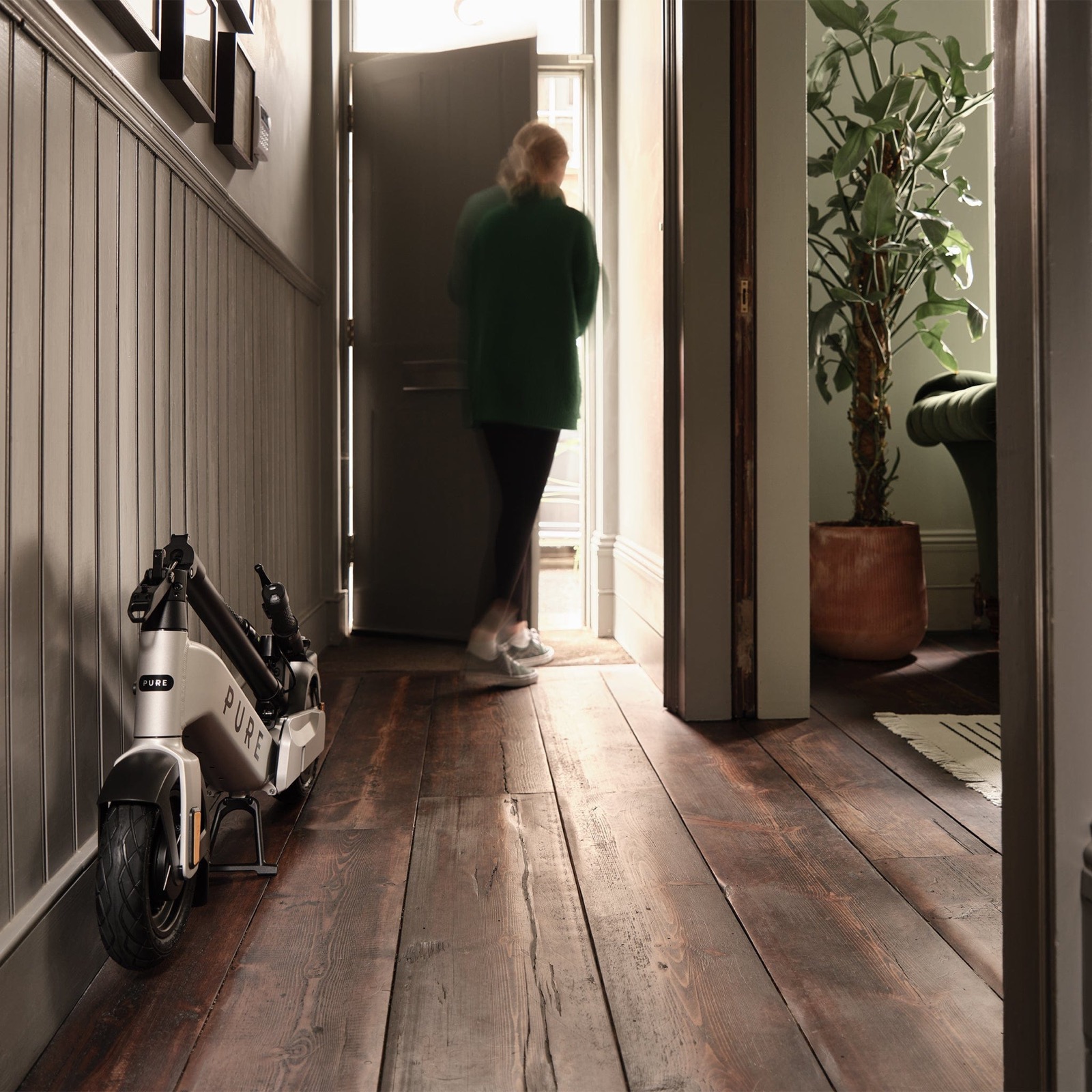 Pure Advance Flex elsparkesykkel sammenlagt og satt i en entré i varmt dagslys